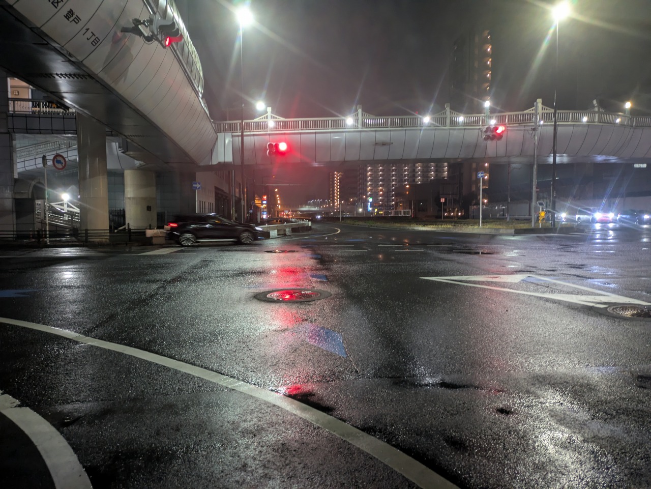 雨で濡れた夜の道路。路面に水が残り、街灯が反射している様子。